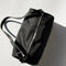 top view of black nylon barrel handbag with leather buckle shoulder strap and trim