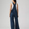 back view of model wearing relaxed fit dark blue overalls with a white tank