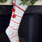 grey cotton stocking with red and white thin stripes, red trim on the cuff and red pom pom detail hanging on a fireplace
