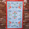 model holding blue tea towel with colorful folk floral print and red trim