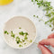 model pulling herbs through cream colored peel, grate, and herb stem remover bowl