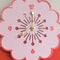 up close of light pink retro daisy shaped clock with mauve trim