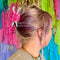 model wearing pink ball of yarn hair claw with two mint knitting needles sticking out