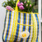front view of blue, white and yellow plaid large recycled plastic tote bag with ric rac detail and egg patch on the front pocket with flowers inside