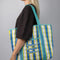 model carrying blue, white and yellow plaid large recycled plastic tote bag with ric rac detail and  embroidered three fishies on the front pocket
