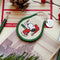 cream patch keychain with green trim and snoopy in a red nightshirt and night cap carrying a candle on a background with pinecone, cranberries and pine branches