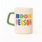 cream ceramic coffee mug with green handle and  colorful 'book person' across the front and smiley face inside