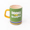 green ceramic mug with yellow handle, rainbow stripe bottom, 'books for breakfast' across the front and 'just a few more pages!' in the inside