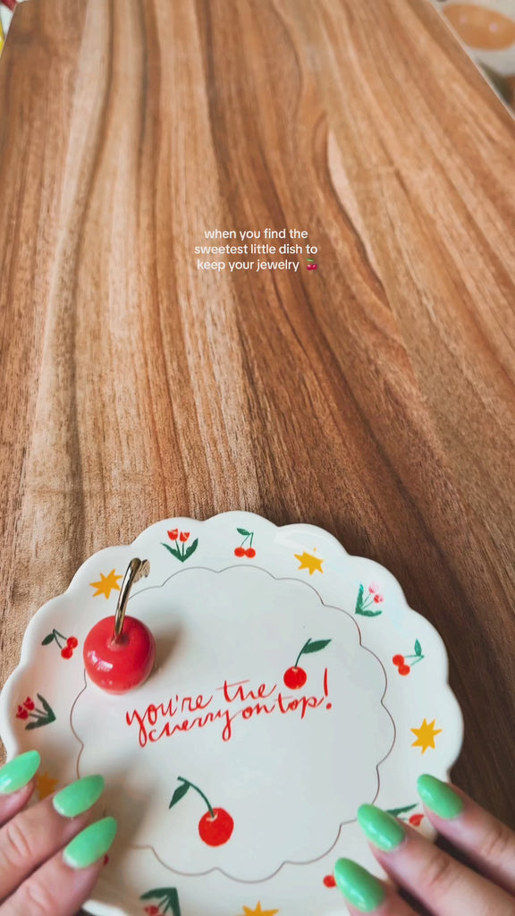 model placing various pieces of jewelry on 'you're the cherry on top' trinket tray with 3D cherry ring holder