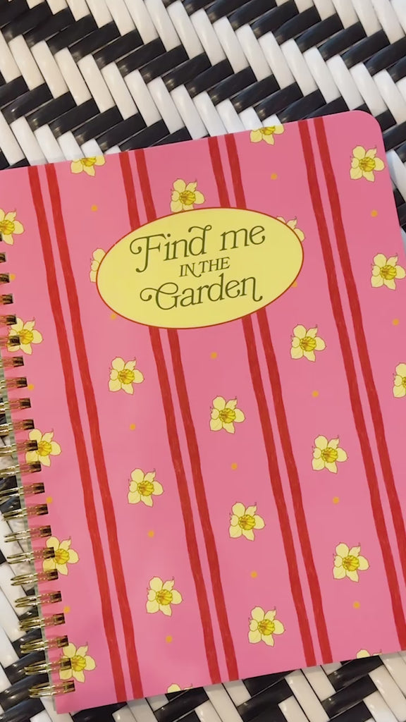 model showing pink mini notebook with vertical double red stripes, realistic daffodil print and cream circle that says 'find me in the garden'