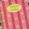 model showing pink mini notebook with vertical double red stripes, realistic daffodil print and cream circle that says 'find me in the garden'