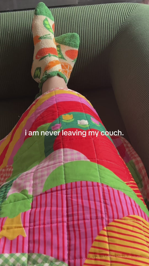model wearing cozy veggie socks and throw blanket and says 'i'm never leaving my couch'