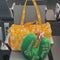 model showcasing yellow duffel bag with retro green, white and orange floral print and green travel neck pillow with white 'what a dream' across the front