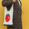 model carrying tote bag that says 'tomatoes are the best' with yellow and red vertical stripes and red handle