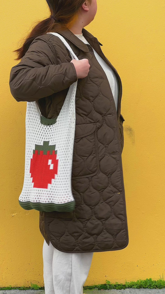 model wearing cream open knit market bag with red tomato in the middle and green trim
