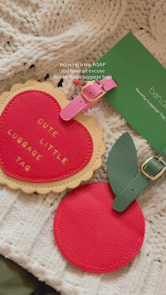 model showcasing set of 2 leatherette luggage tags with red heart that says 'cute little luggage tag' and tag shaped as a cherry