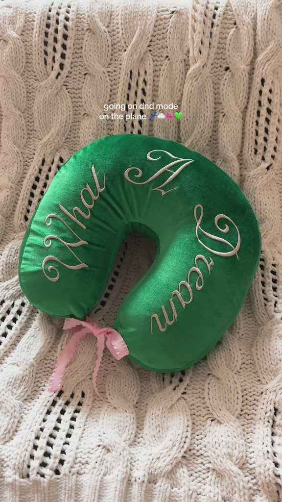 model showcasing green travel pillow with white embroidered 'what a dream' text and pink ribbon
