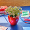 strawberry vase with white flowers on blue surface with desk accessorie scattered throughout